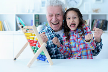 Grandfather teaching his granddaughter to use abacus indoors