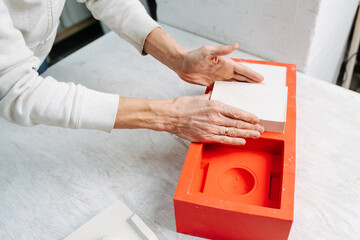 Hands taking freshly made gypsum plaster mold out of the open casting form. Cropped, no face.