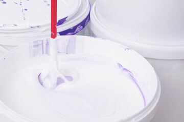 construction mixer stirring purple color in a bucket of white paint, close-up