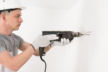 a worker in a helmet makes a hole in a concrete wall with a puncher
