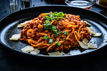 Spaghetti bolognese with minced pork meat and parmesan on black table