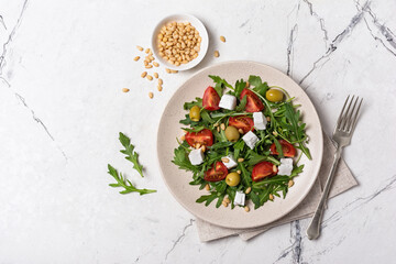 Healthy vegetarian salad with fresh arugula, cherry tomatoes, soft cheese, olives and pine nuts