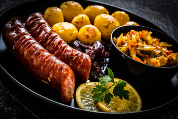 Fried sausages, fried potatoes, onion and fresh vegetables on black table