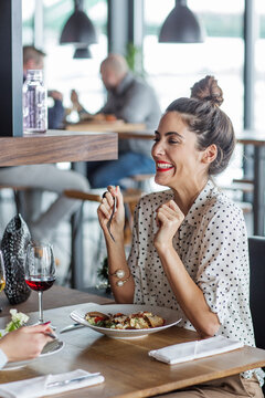 Cheerful businesswoman looking at colleague while having lunch at restaurant