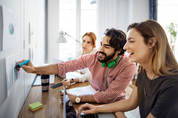 Happy businessman marking on paper while sitting with colleagues in office