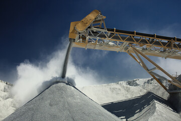 Details of stone crushing equipment at the mining factory in a cloud of dust against the blue sky,...
