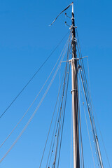 Wooden mast and rigging of a sailing ship against a blue sky