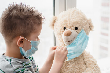 A small child helps a teddy bear put on a medical mask at home in quarantine. Prevention of coronavirus and Covid - 19. Concept