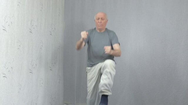 Old man in sportswear performs knee kicks on hands in a jump