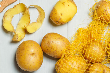 Fresh unpeeled potatoes close-up in the grid and and potato peels on gray wooden background. Natural background with vegetables