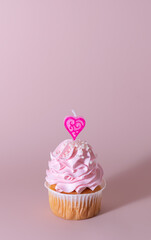 Pink cupcake or muffin for Valentine's Day, Mother's Day or Birthday, decorated with a heart-shaped candle. Place for text. Copy space.