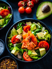 Salmon salad - smoked salmon with avocado and mix of vegetables on black wooden table
