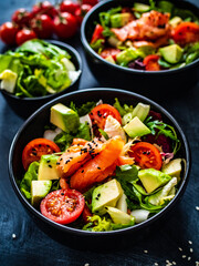 Salmon salad - smoked salmon with avocado and mix of vegetables on black wooden table
