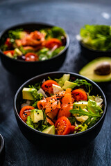 Salmon salad - smoked salmon with avocado and mix of vegetables on black wooden table
