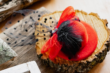 Decorative hat on a hair clip with a red bow and a black veil. Accessory for a themed party or holiday on a natural wooden background