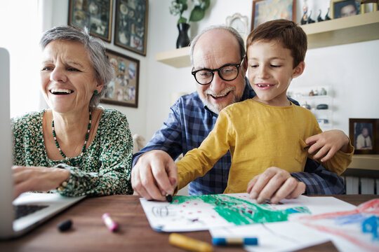 Cheerful grandparents with grandson making drawing at home