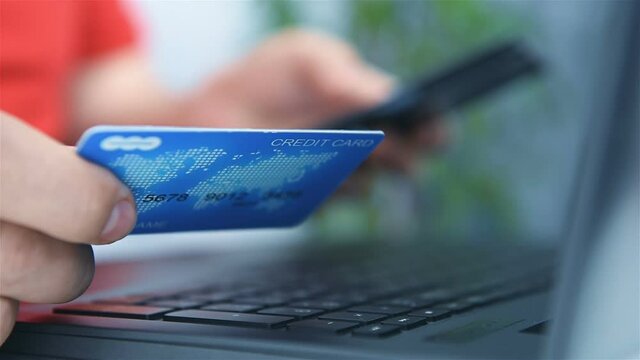 Hands Holding Debit Card And Using On Smart Phone And Laptop. Online Payment And  E-Commerce Concept
