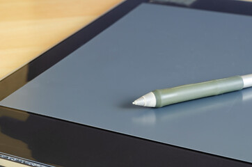 Professional graphics tablet on the table. Fragment of a black tablet and a pen.