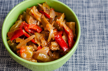 Canned homemade food ready to eat. Canned vegetable salad in a green bowl on a gray-blue background.