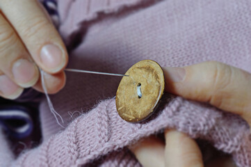 female workers' hands sew a wooden button to a jacket. close-up.
