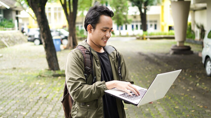 smiling Asian man wearing a backpack with a laptop