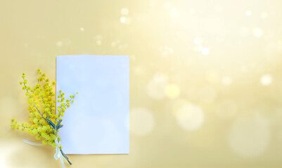 Top view of a white card mockup with mimosa flowers on yellow background. Image with sun flare and bokeh 