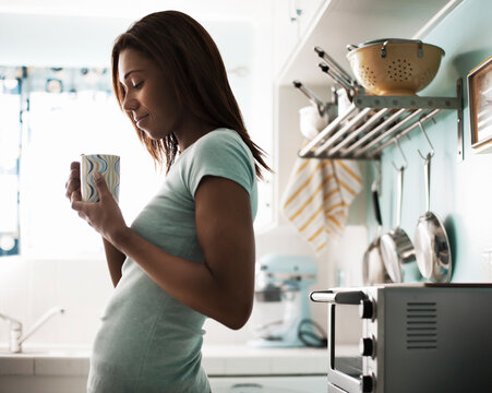 Smiling woman holding coffee cup while standing at kitchen counter