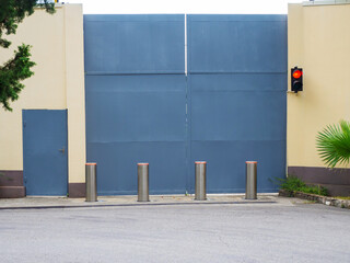 Tall iron gray-blue gate with a traffic light on the wall, automatic retractable bollards and a...