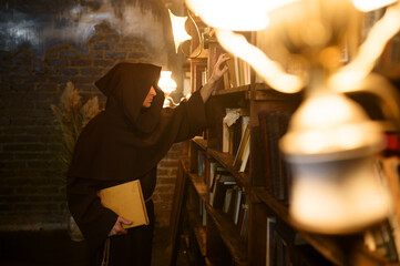 Fototapeta na wymiar Exorcist in black hood choosing book of spells