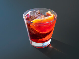 Americano cocktail on black background. Red alcoholic aperitif with orange slice and ice. Classic pre dinner drink, alcoholic beverage.
