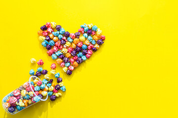 Obraz na płótnie Canvas Colored popcorn. Heart shape made of colored popcorn, flat lay on yellow background with copy space,