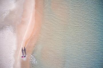 Two people walking along the shore of a beach in the Mediterranean. Xeraco beach, Valencian Community, Spain. Aerial view.