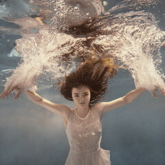 A girl in a white dress posing and somersaulting under water as if flying in zero gravity