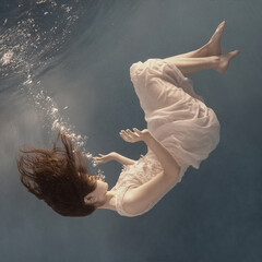 A girl in a white dress posing and somersaulting under water as if flying in zero gravity