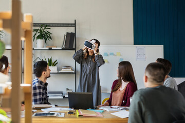 Friends looking at student using virtual reality simulator while sitting in classroom