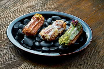 Set of assorted French custard eclairs with custard and assorted toppings served on a black plate on a wooden background. Restaurant food.