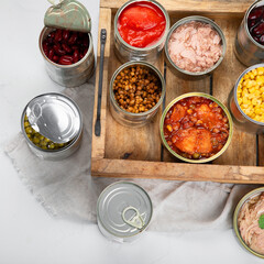 Various canned vegetables, fish and peas in aluminum cans on light gray background.