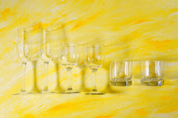 Variety of drinking empty glasses on yellow background with hard shadows and sun glare. sober...