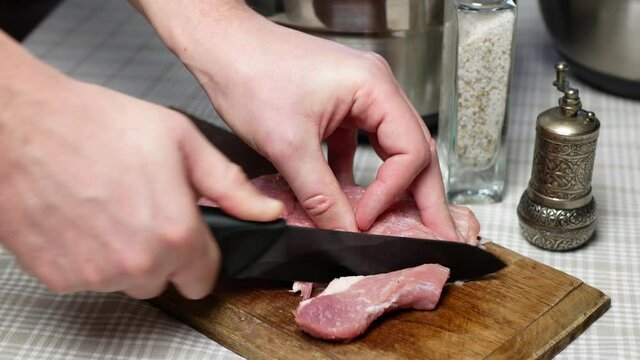 Cutting meat in slices with a black knife. Man cutting fresh raw pork in pieces