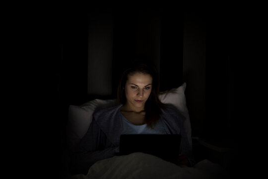 Woman using laptop computer while lying on bed in darkroom