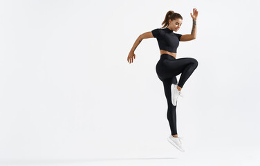 Fit woman exercising indoors. Healthy young female athlete doing fitness workout. Sportswoman in sport clothing jumping on white background, training muscles before running