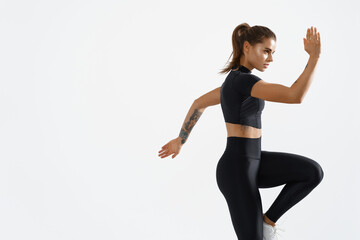 Determined muscular female athlete workout, raising leg and doing stretching exercises. Sport woman in sportswear training indoors, doing fitness aerobics, white background