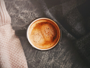 Top view of a black mug of hot, aromatic cinnamon coffee, which is set among warm wool sweaters. Hygge. The cold season and the hot drink.