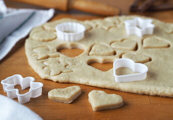 Raw shortbread cookies cut from a layer of dough with cookie cutters on a kitchen board on a dark wooden table.Confectionery background.