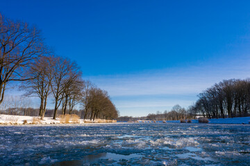 Blauer Himmimel am Wasserkanal, eingefroren im Winter bei eisigen minus Temperaturen in...
