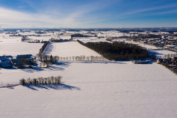 Fototapeta na wymiar Winterlandschaft von Vogelperspektiven über kleine Stadt, Wälder, Ackerflächen, Straßen. Luftaufnahmen am sonnigen Wintertag. 
