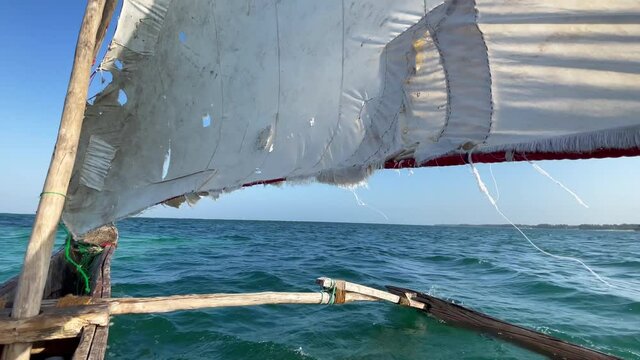 Old traditional maritime traditional vessel Dhow boat sailing under torned sail in the open Indian ocean near Zanzibar island in beautiful sunset time, Tanzania. Traveling 4K footage concept.