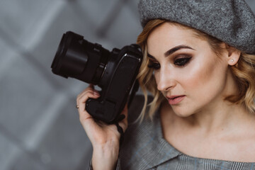 Portrait of a beautiful stylish woman photographer in a gray outfit with a camera in her hands in a photo studio. Soft selective focus. Copy space.