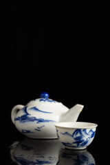 close-up of blue china teapot and cup, on surface with reflection, black background, vertical, with copy space