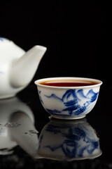Close-up of blue china cup of tea with teapot, with selective focus, black background and reflection, vertical, with copy space
